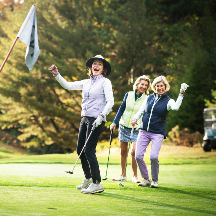 Elliott & Rose navy golf pants with four-way stretch, sleek fit, and subtle piping detail. Women celebrating on the golf course.