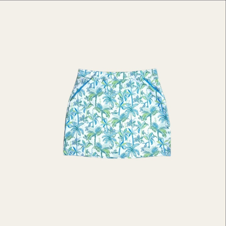 Elliott & Rose white golf skort with green and blue palm tree print, featuring blue pocket piping and elastic waist.