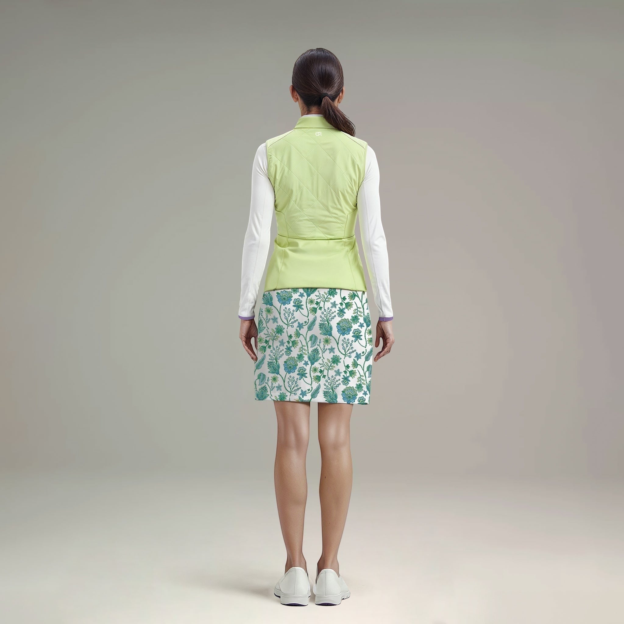 Elliott & Rose quilted chartreuse golf vest with full-zip front and stand-up collar, worn over a white long-sleeve shirt and floral skirt.